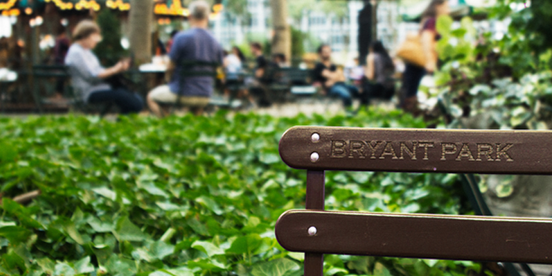 Bench With 'Bryant Park' Imprinted On It With a Crowd and Carousel in the Background