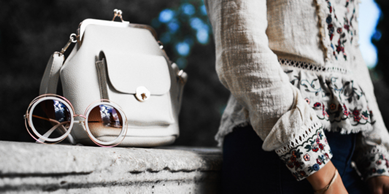 A White Purse and Sunglasses Sit on a Stone Wall Next to Their Owner