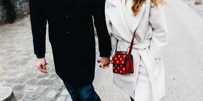 A Couple in Winter Coats Hold Hands as They Walk Down the Street