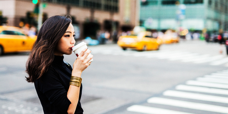 A Young Asian Woman Sips Coffee From a To-Go Cup on a Busy New York City Street