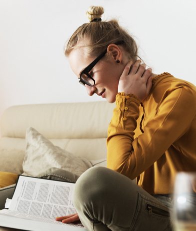 Blonde Woman With Glasses in Yellow Shirt Reads a Book on a White Couch